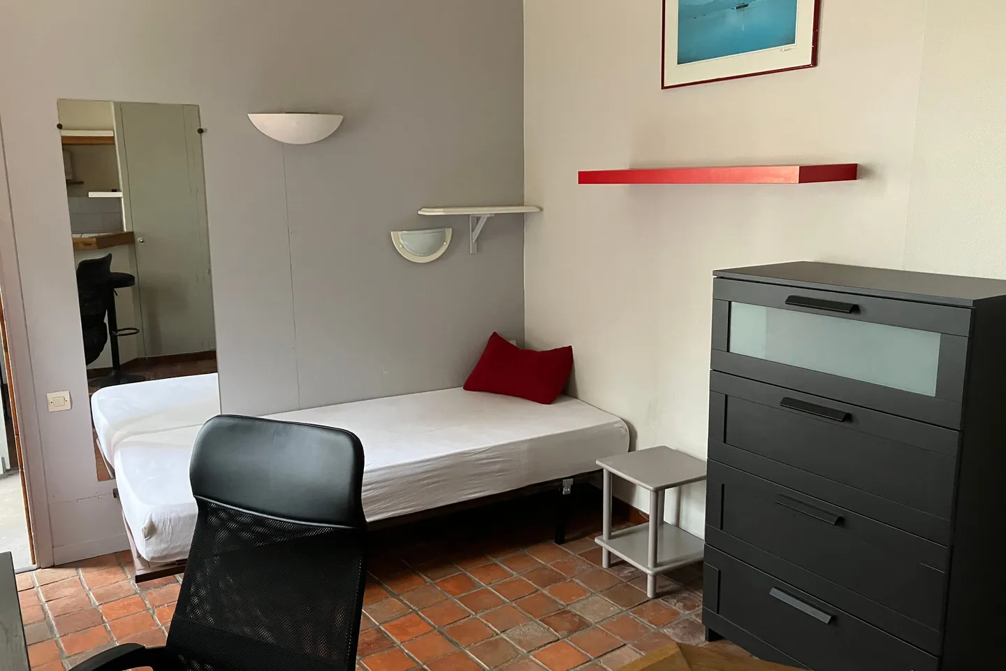 Sleeping area of the studio with bed, chest of drawers and mirror