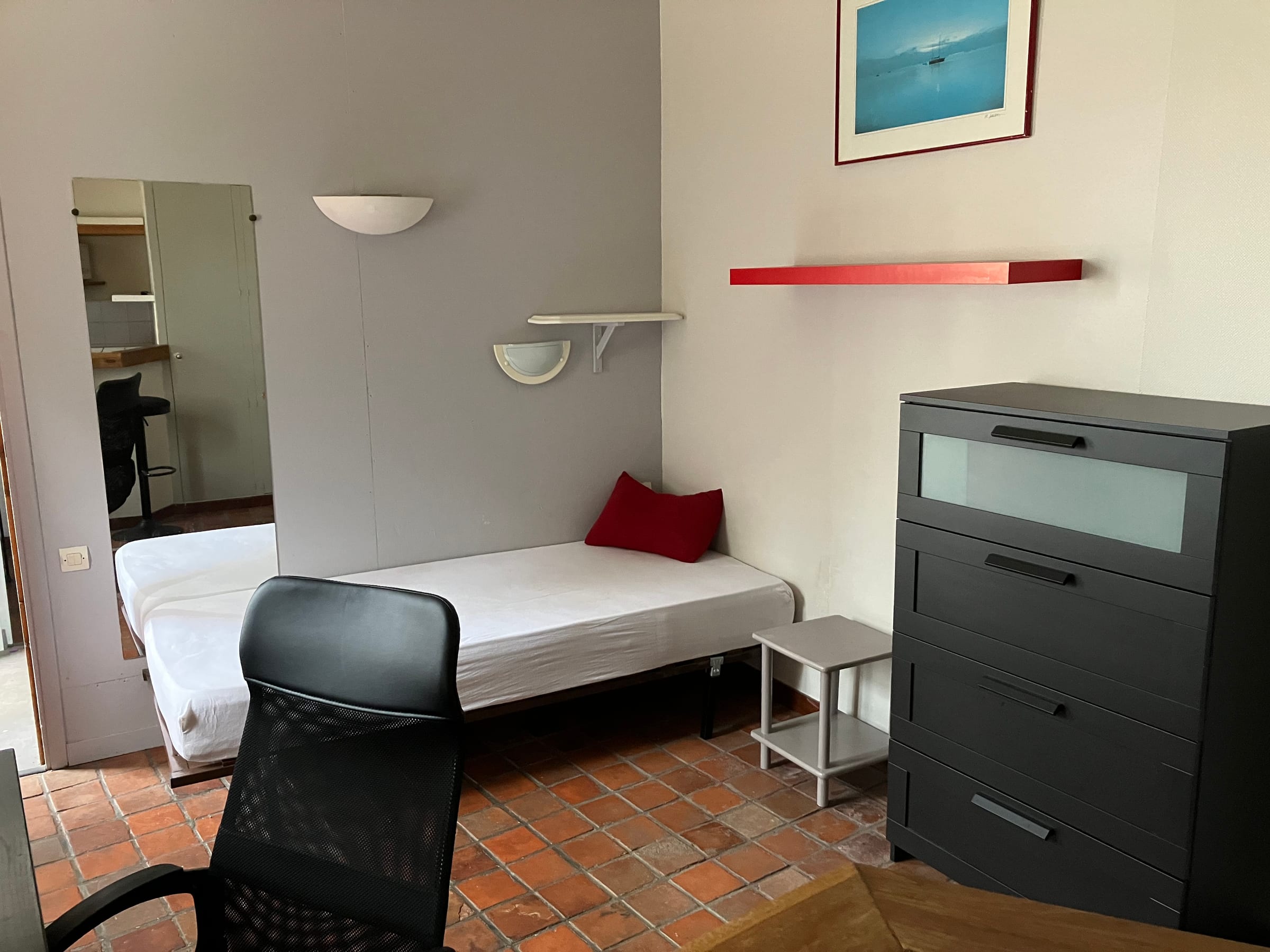 Sleeping area of the studio with bed, chest of drawers and mirror
